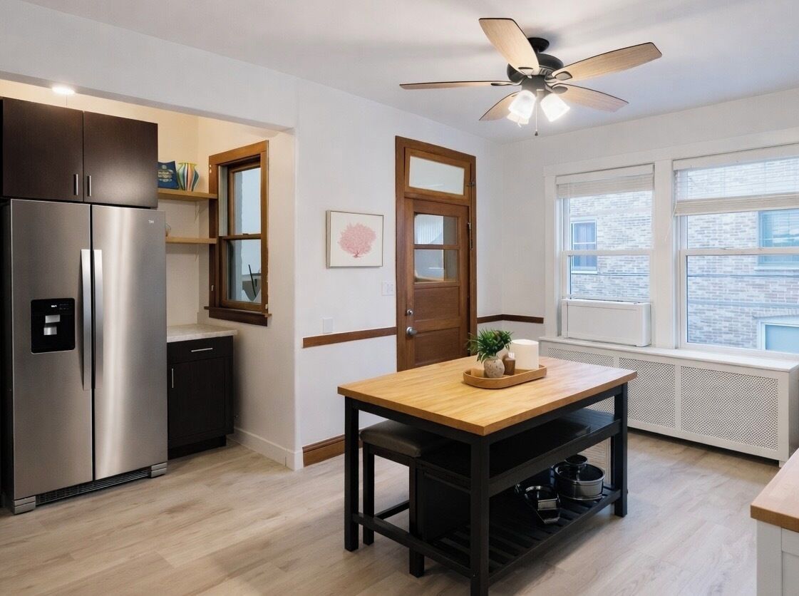 A modern kitchen with a stainless steel refrigerator, a wooden table, and a ceiling fan.