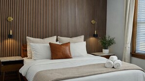 Un dormitorio con una cama, ventilador de techo, mesita de noche, planta en maceta y ventana con cortinas.