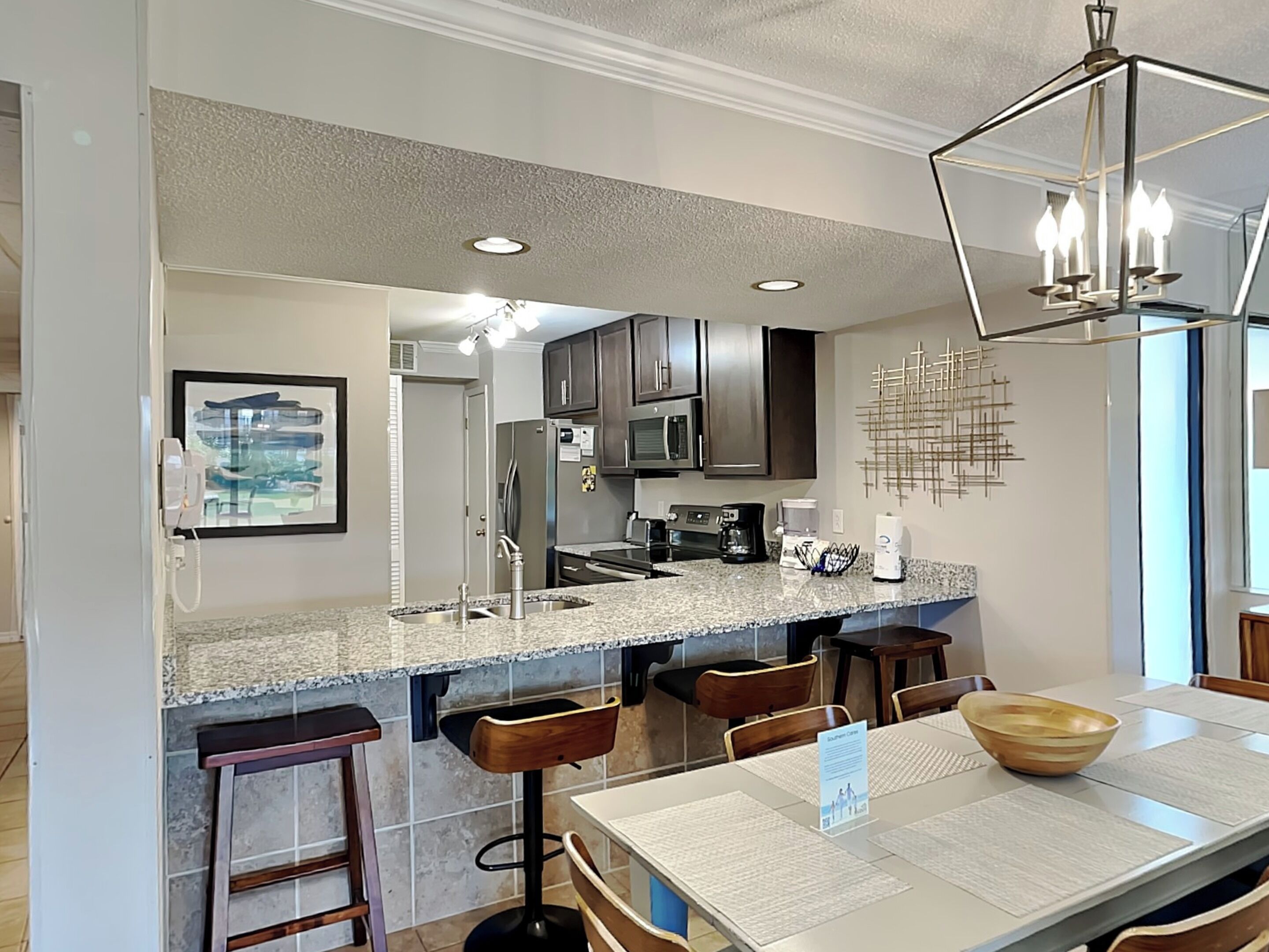 A modern kitchen with granite countertops, stainless steel appliances, and a bar area with stools.