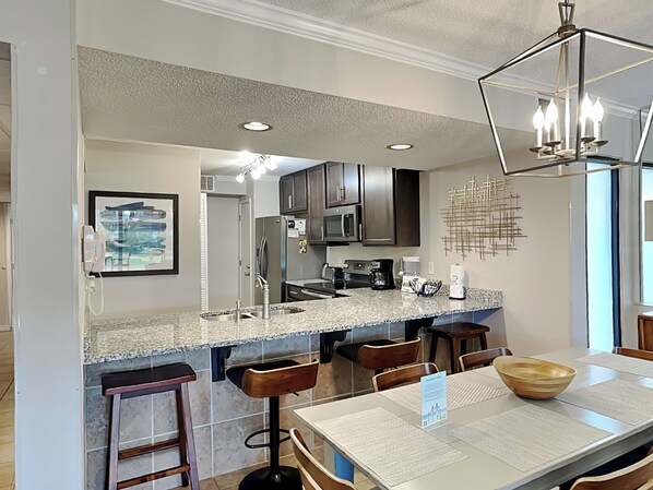 Cozinha moderna com bancadas de granito, eletrodomésticos de aço inoxidável e um espaço bar com banquetas.