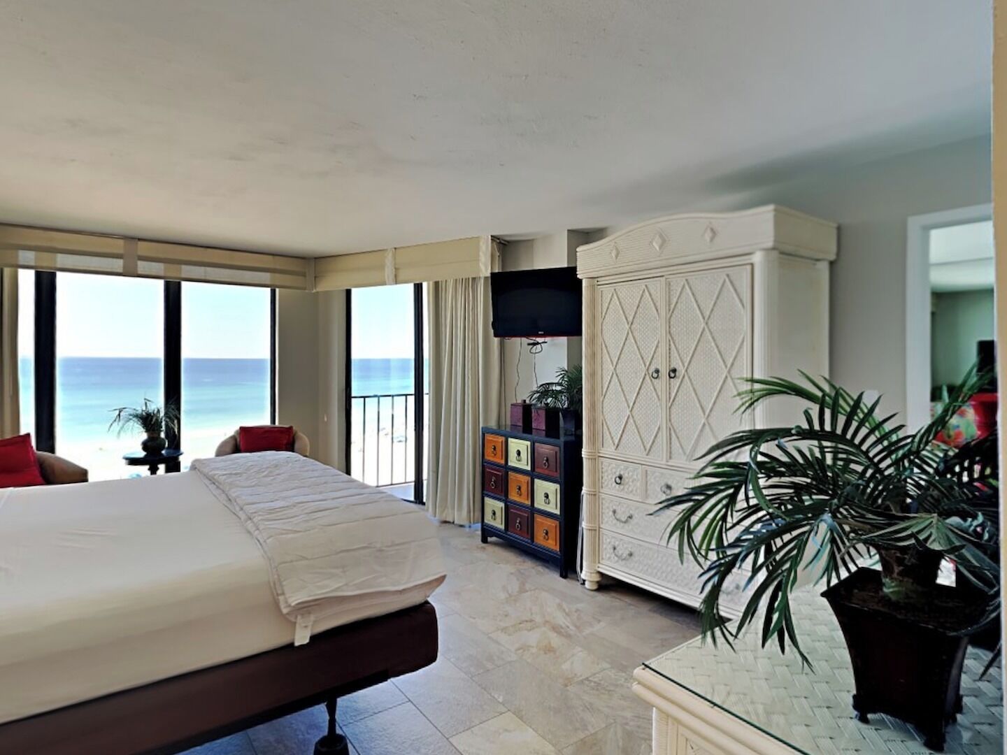 A bedroom with a large bed, a wardrobe, a TV, and a view of the ocean.