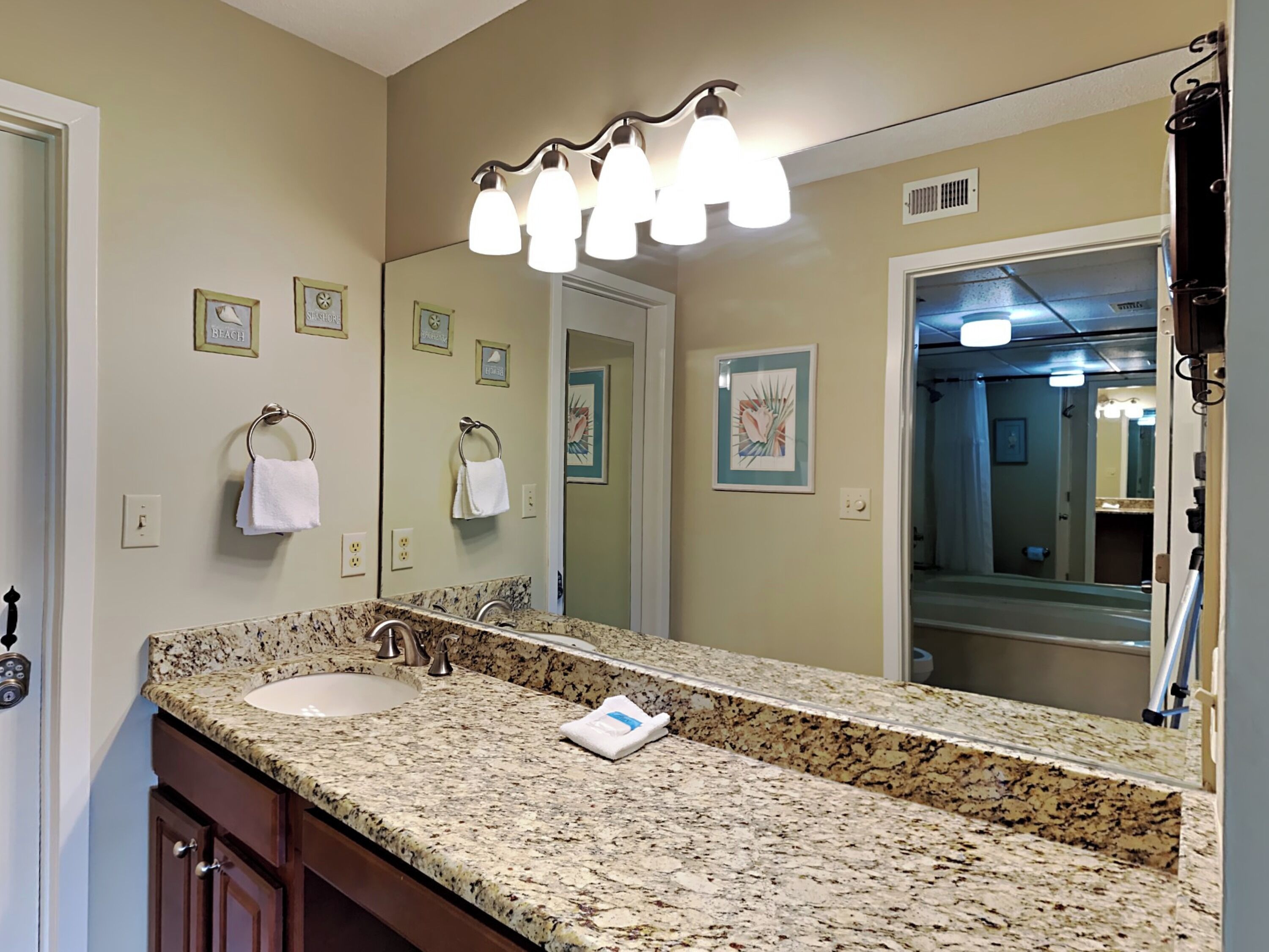 A bathroom with a granite countertop, two sinks, a large mirror, and a towel rack.