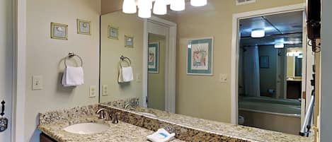 A bathroom with a granite countertop, two sinks, a large mirror, and a towel rack.