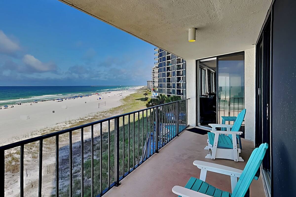 Een balkon met uitzicht op een strand en de oceaan, voorzien van een leuning en twee stoelen.