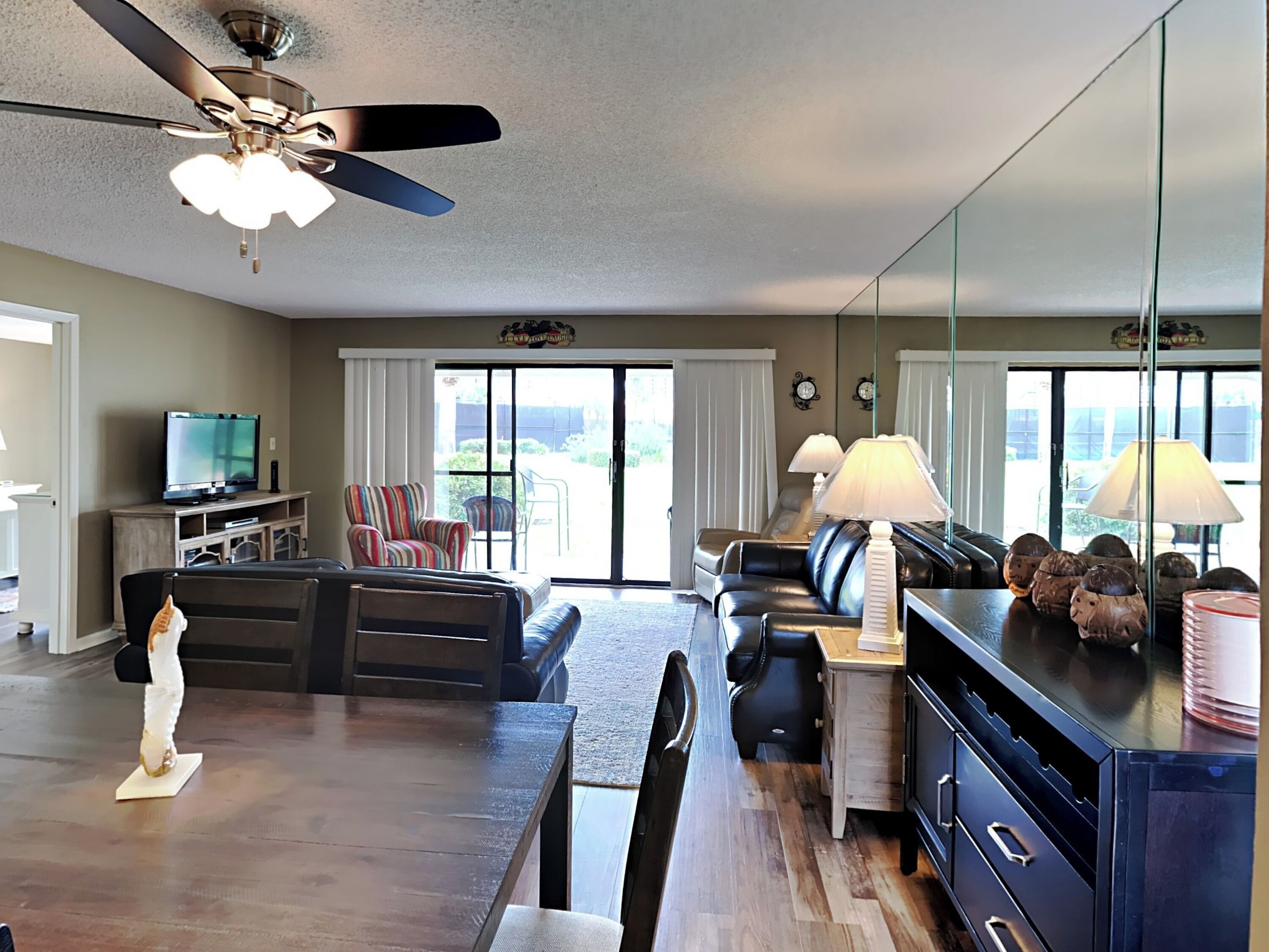 A spacious living room with a wooden dining table, a black leather sofa, a striped armchair, and a television.