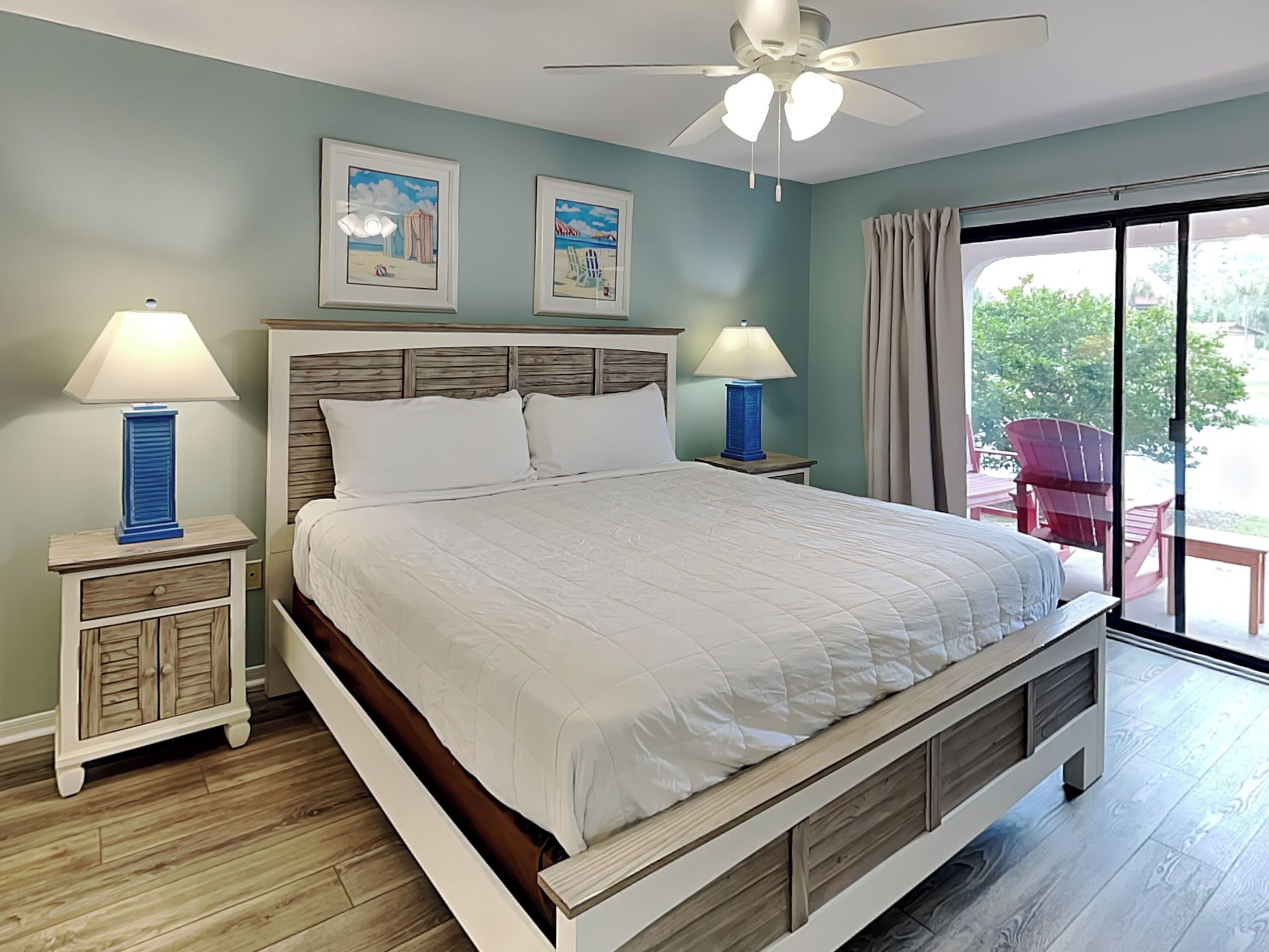 Un dormitorio con cama, dos mesitas de noche, ventilador de techo y un ventanal con cortinas.