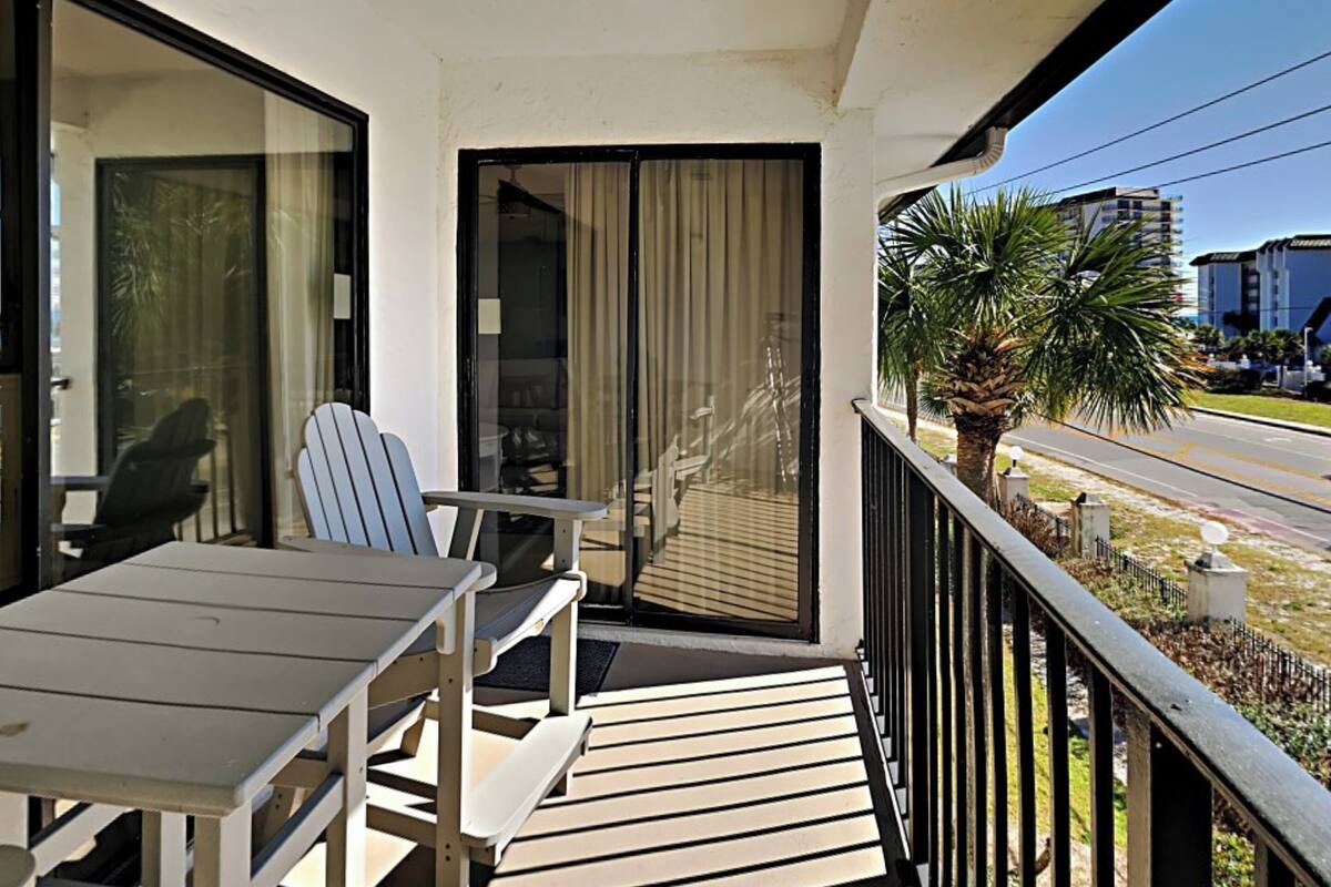 Een balkon met een tafel en stoelen, een schuifdeur en uitzicht op een palmboom en gebouwen.