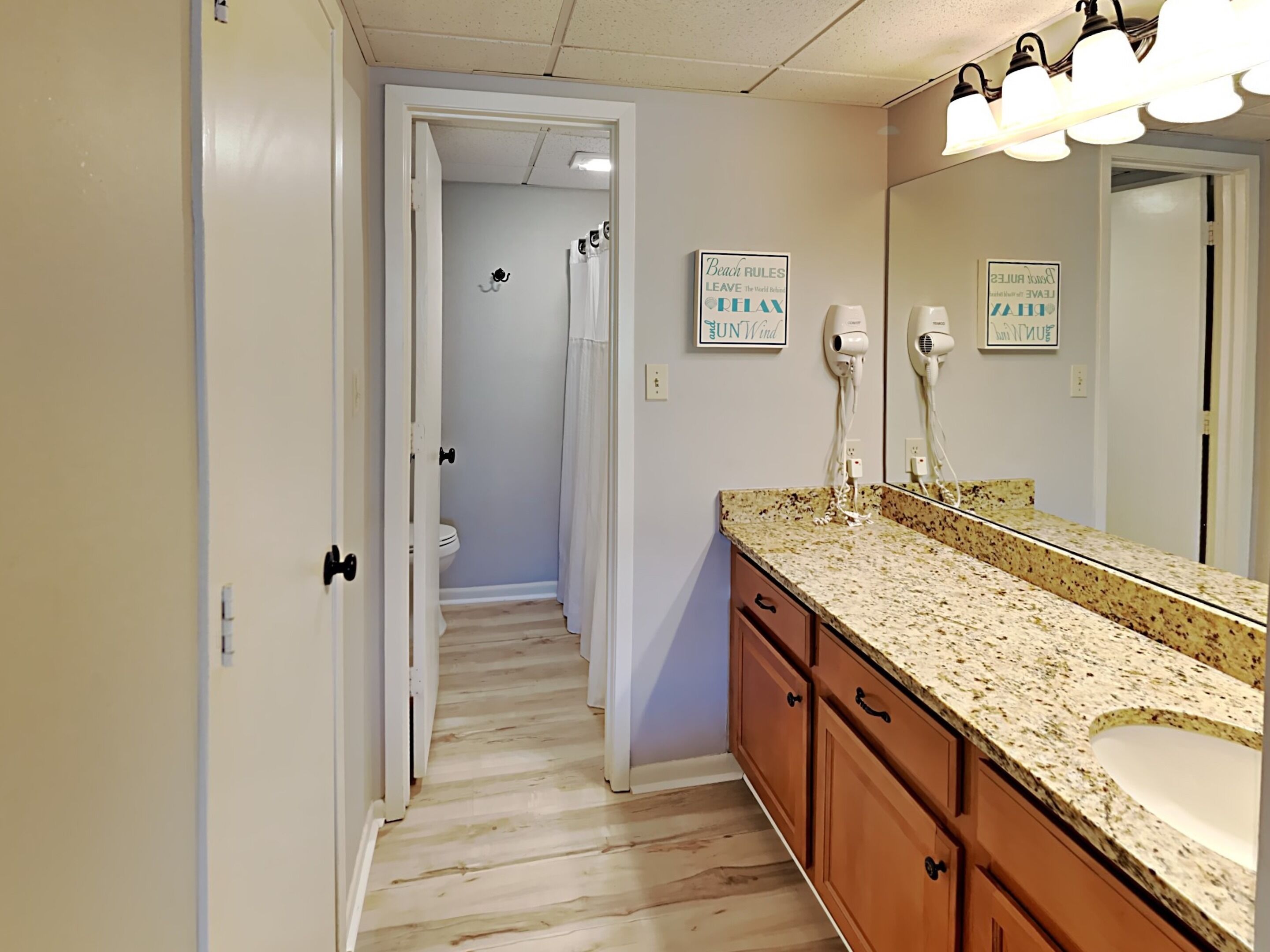 A bathroom with a wooden floor, a sink, a mirror, and two hair dryers on the wall.