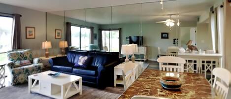 A living room with a blue sofa, white coffee table, and a dining area with a marble table and white chairs.