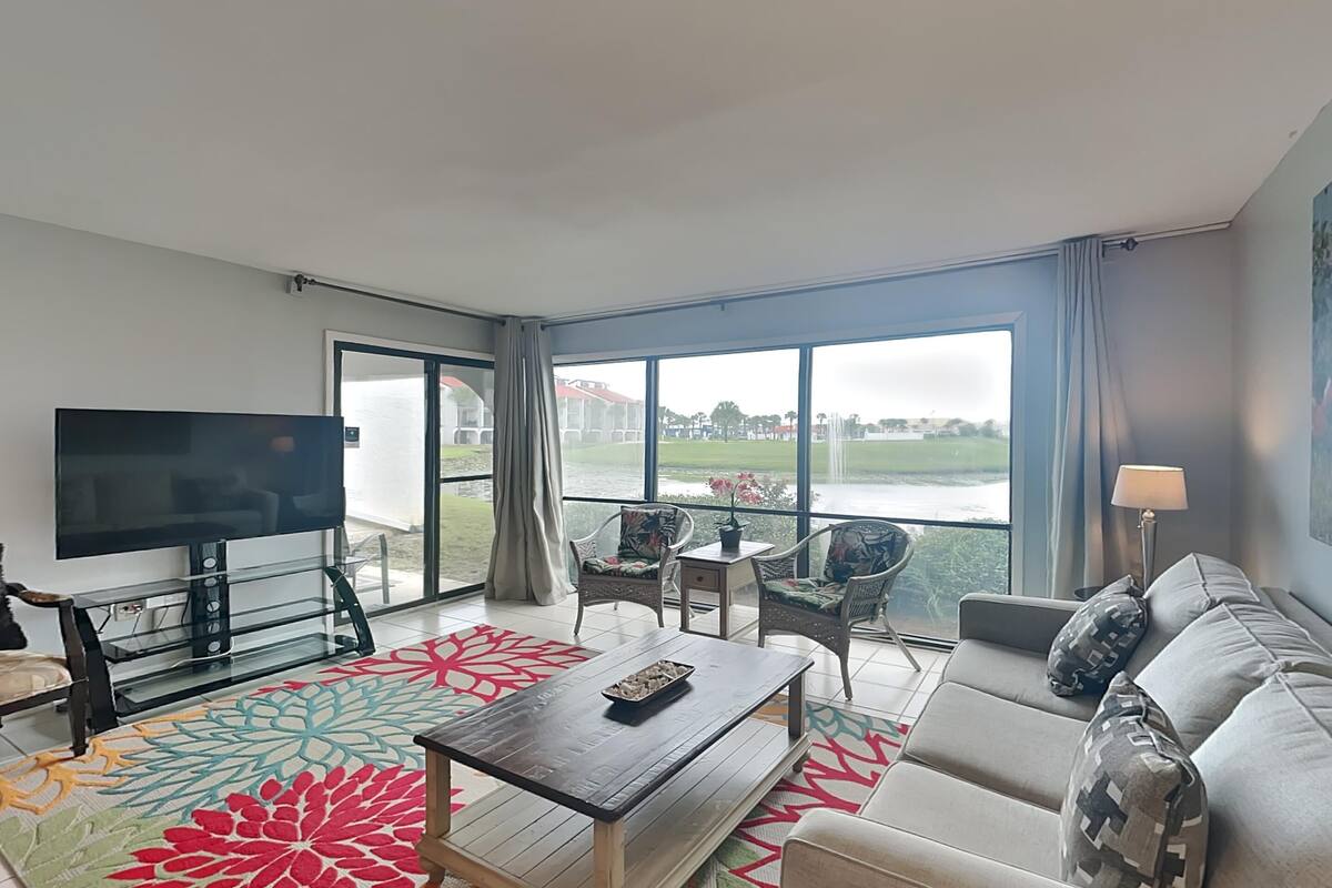 Een moderne hotelkamer met een groot raam, een flatscreen televisie, een bank, een salontafel en een kleine tafel met stoelen.