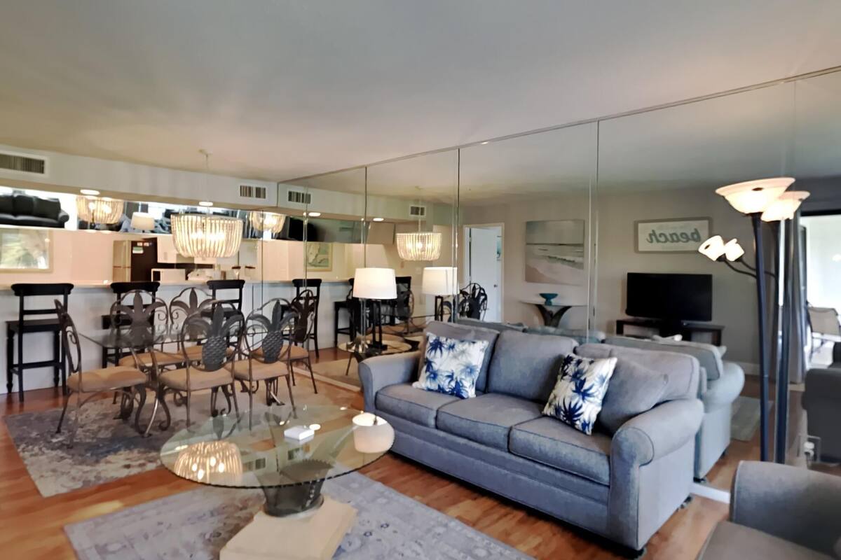 Een moderne woonkamer met een grijze bank, een glazen salontafel en een eethoek met stoelen en een tafel.