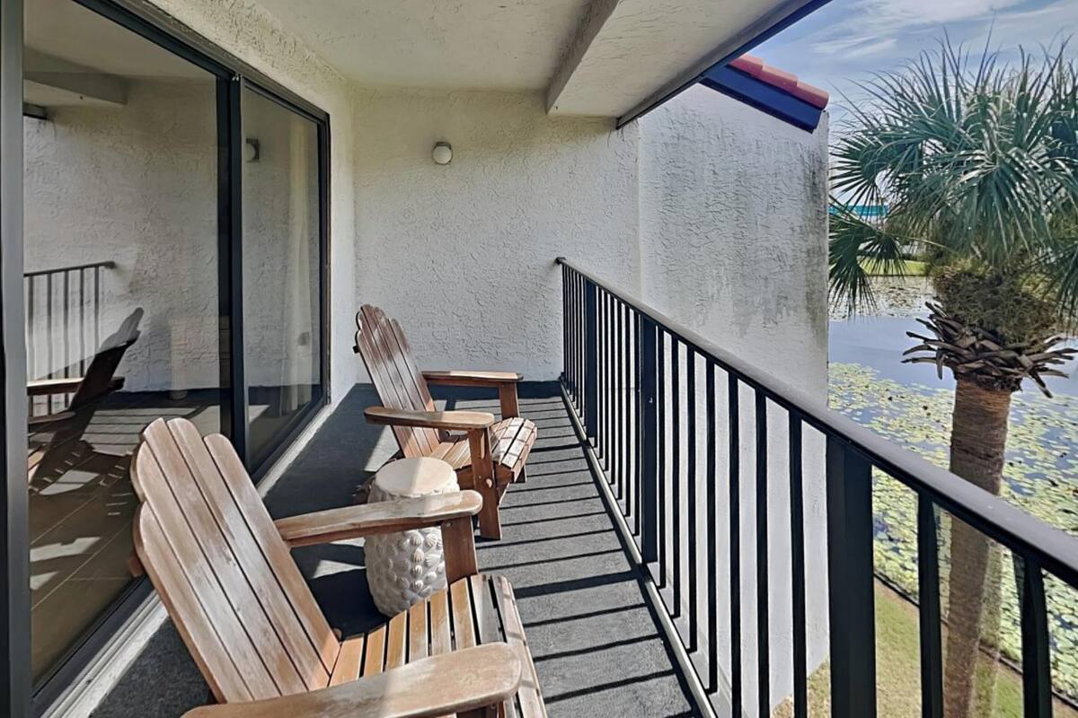 Een balkon met houten stoelen en een tafel, met uitzicht op een waterpartij met een palmboom.