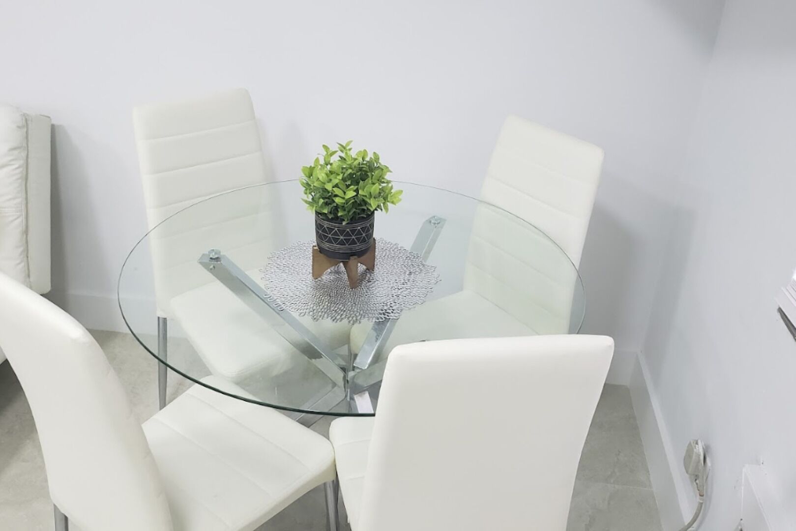 A round glass table with a potted plant in the center, surrounded by white chairs.