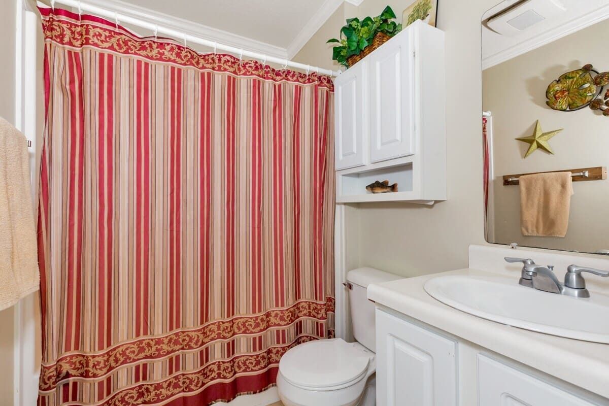 A bathroom with a striped shower curtain, a white toilet, a sink with a mirror, and a star decoration on the wall.