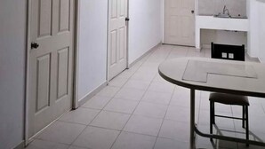 A room with white walls, a tiled floor, a round table with a chair, and two white doors. - departamento bonito en linares NL (Linares)