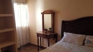 A bedroom with a bed, a wooden headboard, a bedside table with a mirror, and a wardrobe. - departamento bonito en linares NL (Linares)