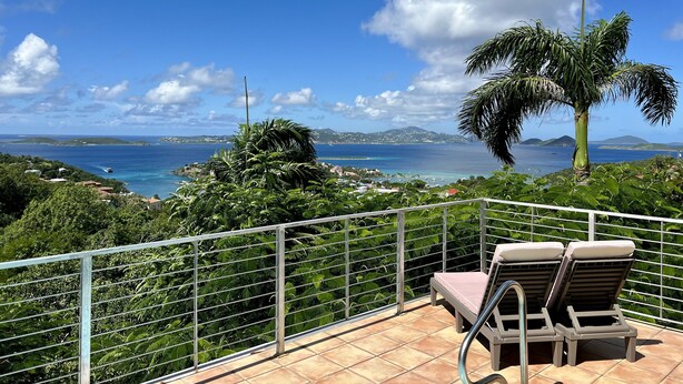 A balcony with two lounge chairs, a metal railing, and a view of the sea and distant hills. - Ylang Ylang Luxury 2 Suite Villa - Cruz Bay, St. John (Cruz Bay)