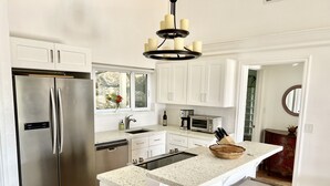 A modern kitchen with white cabinetry, stainless steel appliances, a central island with stools, and a chandelier. - Ylang Ylang Luxury 2 Suite Villa - Cruz Bay, St. John (Cruz Bay)