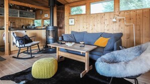 A cozy cabin interior with a wooden ceiling, a sofa, a rocking chair, a dining table, and a fireplace. - The Secret Cabin with hot tube in nature reserve close to Reykjavik  (Hafnarfjordur)
