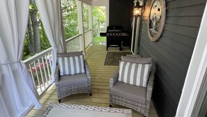 Eine überdachte Veranda mit Korbmöbeln, einem Grill und einem dekorativen Wandelement.