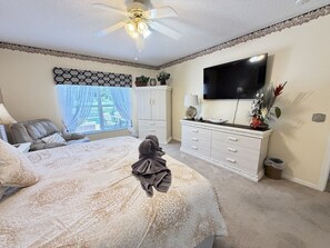 A bedroom with a bed, a ceiling fan, a TV, a dresser, and a window with curtains. - Luxury Lakeside Pool & Spa Home close to Disney (Kissimmee)