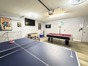 A room with a ping pong table, a pool table, and a foosball table.