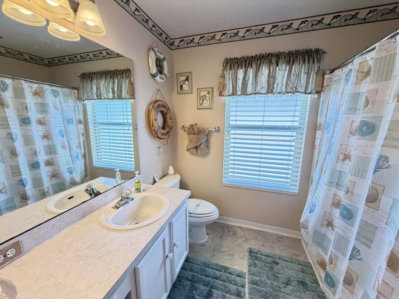 A bathroom with a double sink vanity, a toilet, and a shower curtain with a nautical theme.