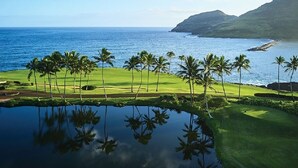 A golf course with a pond reflecting palm trees and a view of the ocean and mountains. - Modern Oceanfront Resort Living. Luxury Oceanfront Bedroom Suites. Sleeps 10! (Lihue)