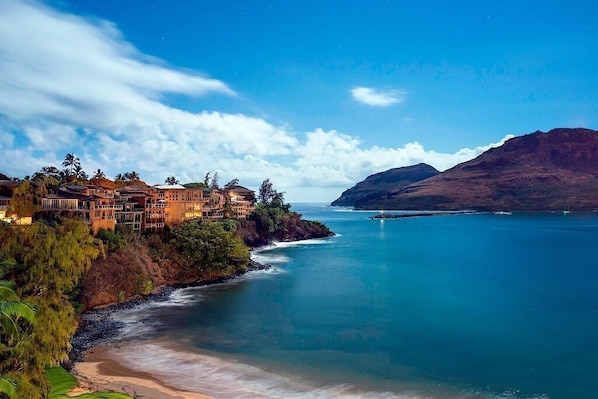 Un hôtel situé sur la côte, composé de plusieurs bâtiments, avec une plage et une montagne en arrière-plan.
