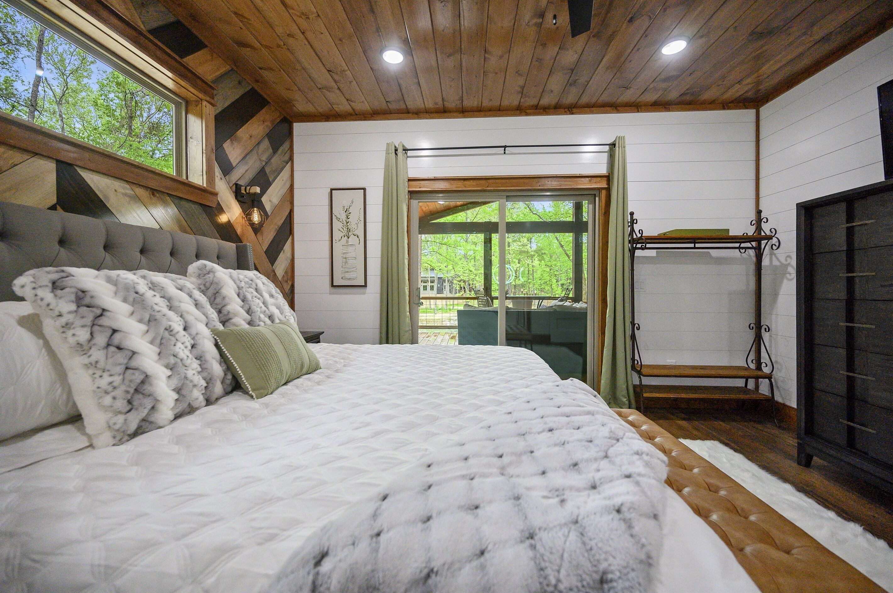Un dormitorio con una cama grande, techo de madera y vistas al exterior a través de una ventana.