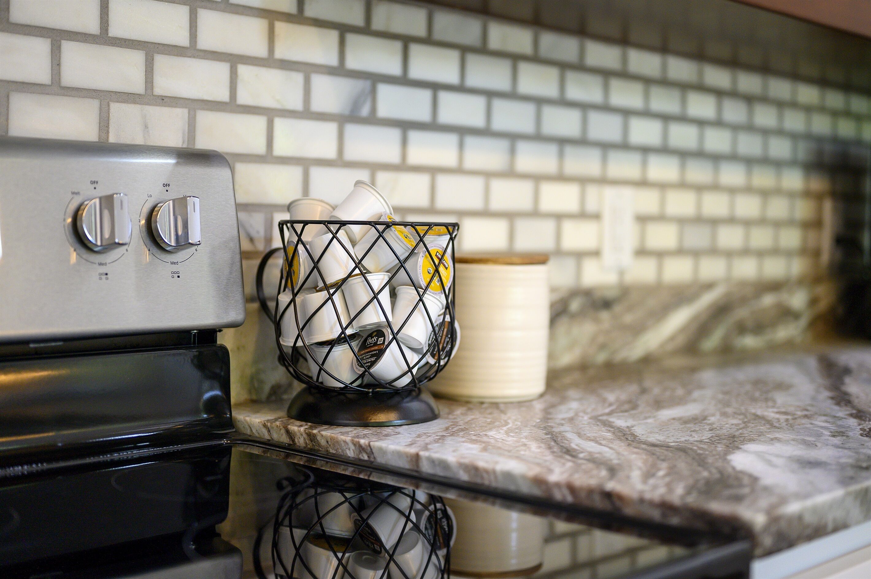 A kitchen with a stove, a wire basket with dishes, and a tiled backsplash.