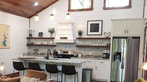 A modern kitchen with white cabinetry, a marble island, and a stainless steel refrigerator. - Couple's Escape + King Bed + Fountain + Hot Tub (Broken Bow)