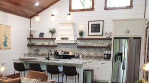 A modern kitchen with white cabinetry, a marble island, and a stainless steel refrigerator. - Couple's Escape + King Bed + Fountain + Hot Tub (Broken Bow)