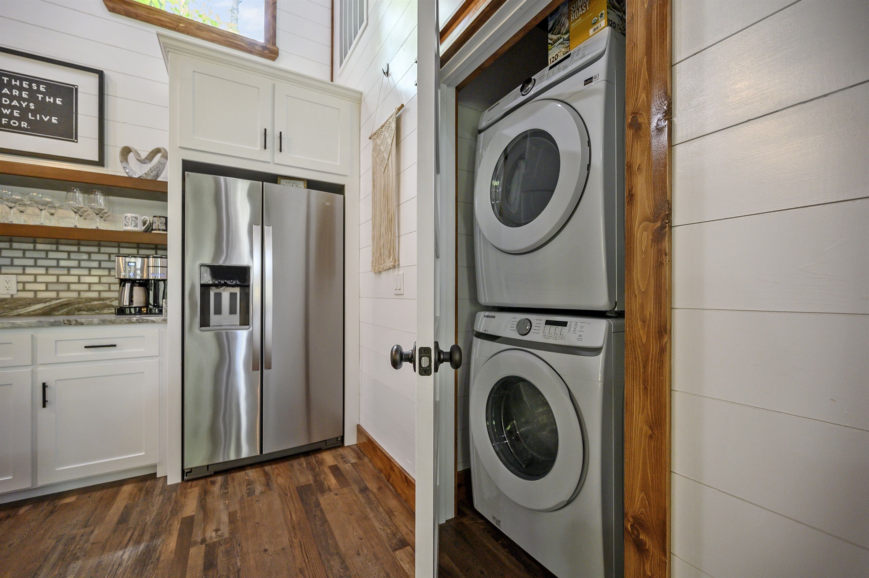 A compact kitchen with a stainless steel refrigerator, a double washer and dryer unit, and a coffee maker on the counter.