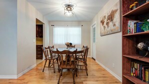 A dining area with a round table and wooden chairs, a bookshelf with books, and a world map painting on the wall. - Family Fun at Primrose Retreat - Cozy, Clean & Chemical-Free (Republic)
