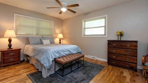 A bedroom with a bed, two bedside tables with lamps, a bench, a dresser, and a ceiling fan. - Family Fun at Primrose Retreat - Cozy, Clean & Chemical-Free (Republic)