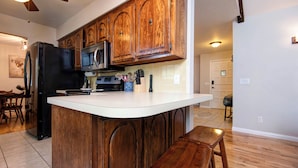 A kitchen with wooden cabinets, a black refrigerator, a microwave, and a stove. There is a white countertop and a wooden bench. - Family Fun at Primrose Retreat - Cozy, Clean & Chemical-Free (Republic)