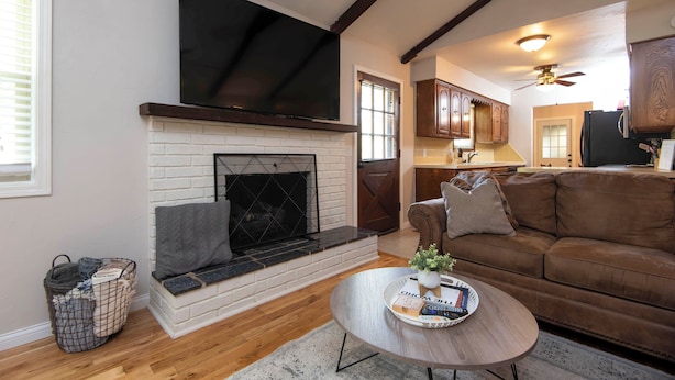 A living room with a fireplace, a television mounted above it, a brown leather sofa, and a coffee table with a tray. - Family Fun at Primrose Retreat - Cozy, Clean & Chemical-Free (Republic)