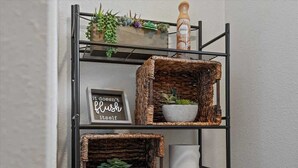 Une étagère en métal avec des paniers en osier contenant des plantes et un panneau encadré.