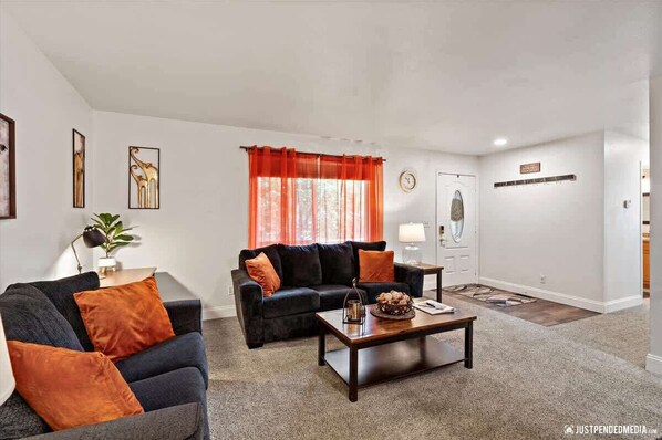 A living room with a dark sofa, a coffee table, and a red curtain. - Alaska Windflower Escape (Anchorage)