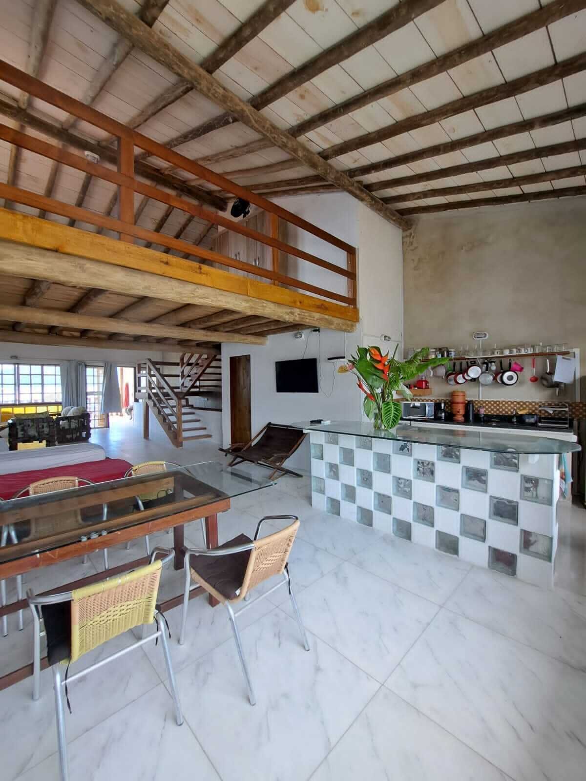 Una cocina amplia con techo alto, un comedor con mesa de vidrio y una pequeña isla con utensilios de cocina.