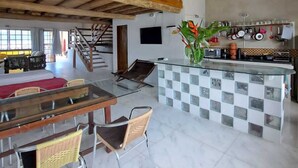 A spacious kitchen with a high ceiling, a dining area with a glass-top table, and a small island with kitchen utensils. - Paraty house near historic center (paraty)