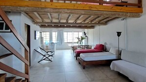 A spacious room with a high ceiling, a loft bed, a sofa, a dining table, and a chair. - Paraty house near historic center (paraty)