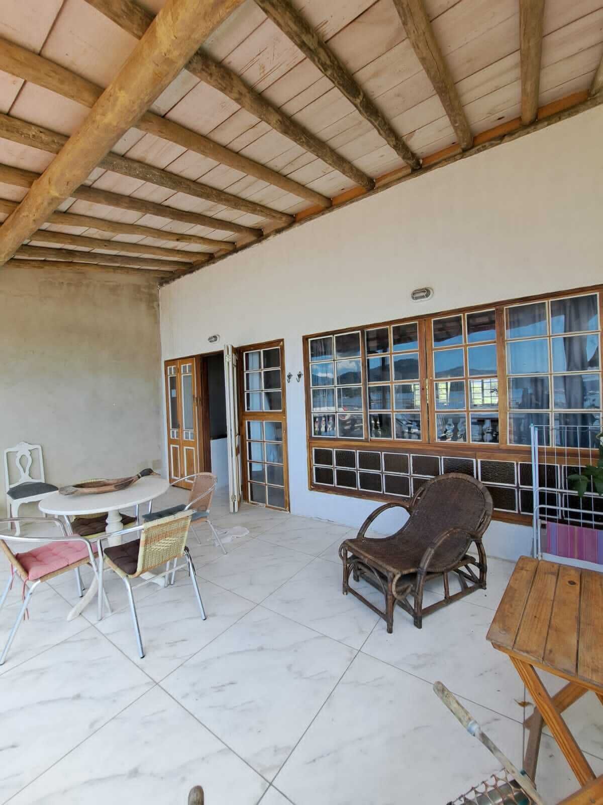 Un amplio patio con suelo de baldosas, mobiliario de madera y grandes ventanales que ofrecen vistas al exterior.