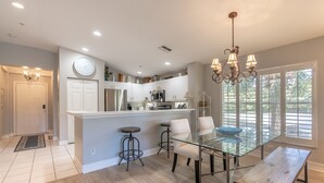 A modern kitchen with white cabinets, a central island, and a dining area with a glass table and metal chairs.
