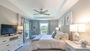 A bedroom with a bed, a TV, a ceiling fan, and a window with curtains.