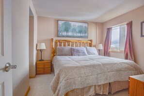 Een slaapkamer met een groot bed, twee nachtkastjes met lampen, een raam met gordijnen, en een schilderij aan de muur.