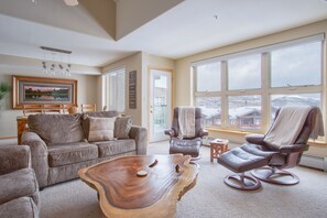 Relax in this cozy living space with a high ceiling and large windows offering a view of the surrounding landscape.