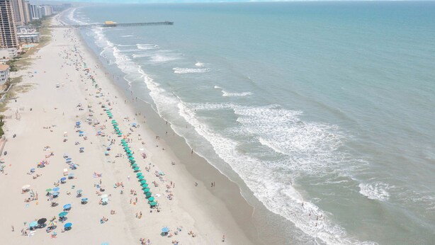 Ein Strand mit mehreren Reihen von Sonnenschirmen und Personen.