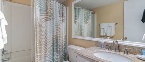 A bathroom with a shower, toilet, sink, and a mirror.